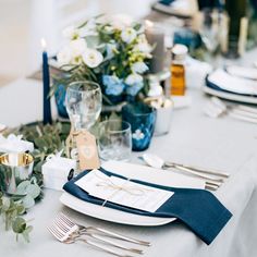 the table is set with blue and white plates, silverware, napkins, and candles