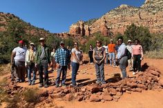 a group of people standing on top of a dirt field next to trees and mountains