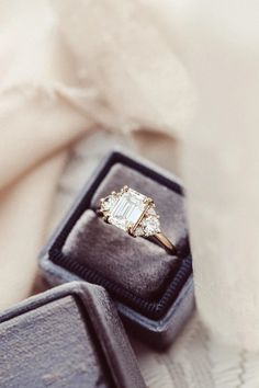 an engagement ring in a velvet box on top of a white cloth covered tablecloth