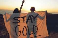 two people standing on top of a hill holding up a sign that says stay gold