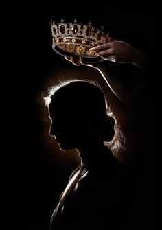 the silhouette of a woman holding a crown over her head in front of a dark background