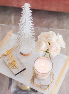 a small white christmas tree sitting on top of a glass table next to a candle