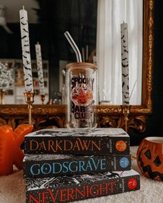 three books stacked on top of each other in front of a mirror with candles and pumpkins