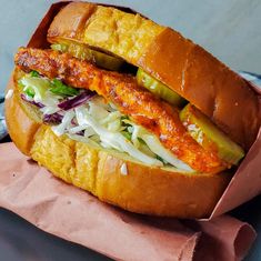 a sandwich with meat and vegetables in it on a piece of wax paper next to a fork