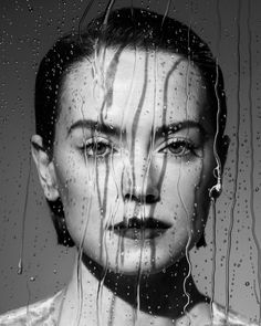 a woman's face is seen through the rain drops on a glass window as she stares into the distance