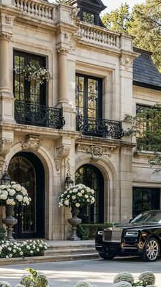 a black car parked in front of a large building with white flowers on it's balconies