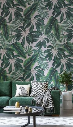 a living room with green couches and tropical wallpaper