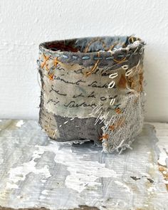 a cup that is sitting on top of a piece of wood and has torn up fabric