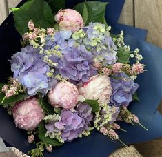 a bouquet of purple and white flowers sitting on top of a blue vase filled with greenery