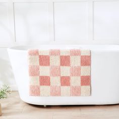 a bath tub with a red and white checkered towel on the side, next to a potted plant