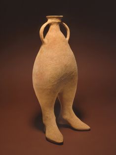 an old clay vase sitting on a brown surface with one leg bent down and the other standing up