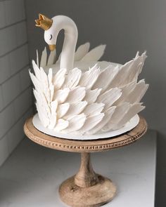 a white swan cake sitting on top of a wooden stand next to a tiled wall