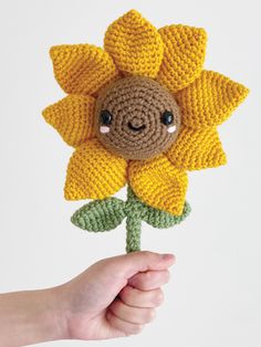 a crocheted sunflower with a smiley face on it's center being held by a hand