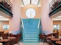 a clock is on the wall next to some tables and chairs in a room with pink walls