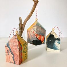 three small boxes are hanging from a tree branch and decorated with colored paper, which has been cut out to look like houses