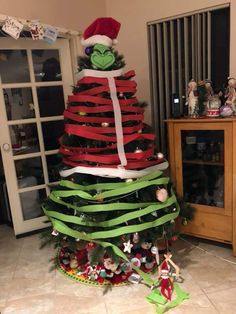 a christmas tree decorated with green and red ribbon, the grin's hat is on top