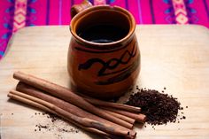 cinnamon sticks and spices sit on a cutting board next to a cup of black coffee