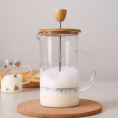 a glass coffee pot filled with white liquid on top of a coaster next to bread