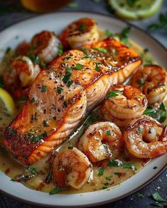 a white plate topped with fish and shrimp next to lemon wedges, garnished with parsley