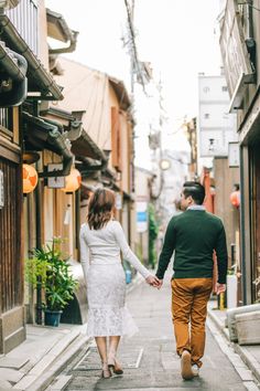 a man and woman holding hands while walking down an alleyway in the middle of town