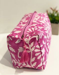 a pink and white bag with a tasseled handle sitting on a table next to a potted plant