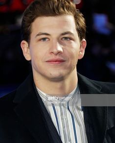 a young man in a black jacket and striped shirt is looking at the camera while smiling