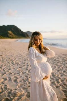 a pregnant woman in a white dress standing on the beach