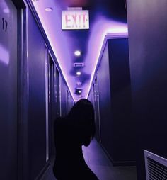 a dark hallway with purple lighting and exit signs on the walls, along with a woman's silhouette