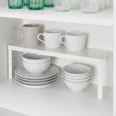 white dishes and cups are stacked on the shelf