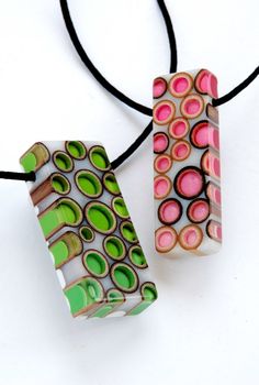 two pieces of glass sitting on top of a black cord necklace with pink, green and white designs