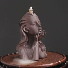 a statue of a woman with her eyes closed and hands clasped to her face, sitting on a round wooden table