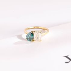 an emerald and diamond ring sitting on top of a white surface