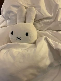 a white stuffed animal laying in a bed under a blanket with eyes drawn on it