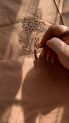 a woman is drawing flowers on a piece of fabric with a pencil and scissors in her hand