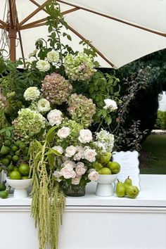 an arrangement of flowers and fruit is on display at a garden show in front of a white umbrella