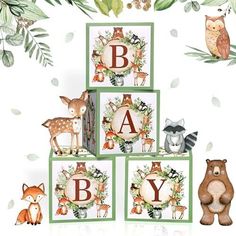 woodland baby blocks with animals and letters on them, surrounded by greenery leaves in front of a white background