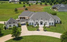 an aerial view of a large white house in the middle of a green field with lots of trees