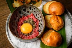 an egg on top of some meat in a bowl next to rolls and other food