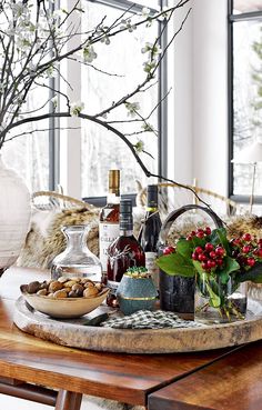 a wooden table topped with bottles of wine and flowers next to a vase filled with berries