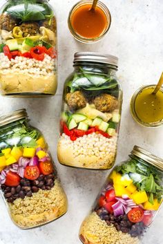 four mason jars filled with different types of salads and dressing sauce on a white surface