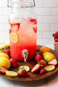 a pitcher filled with lemonade and strawberries on top of a wooden platter