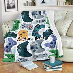 a blanket with video game controllers on it is sitting next to a couch and books