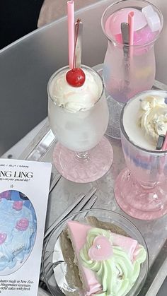 three desserts are sitting on a tray next to a book and drink glasses with strawberries in them