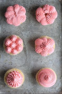 pink frosted cupcakes sitting on top of a baking sheet