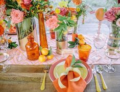 the table is set with orange and pink flowers in vases, plates, silverware, and utensils