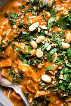 a bowl filled with chicken and spinach covered in sauce, garnished with peanuts