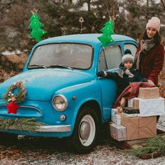 a woman standing next to a small blue car with presents on the hood and trunk