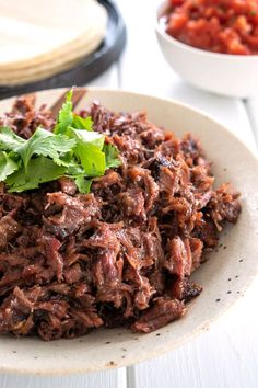 a white plate topped with shredded meat and garnished with cilantro