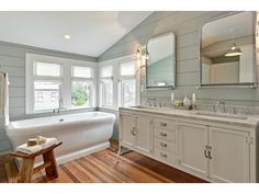 a large white bathroom with wood flooring and two sinks on the vanity next to the bathtub