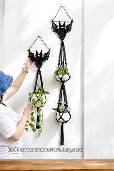 a woman hanging plants on the side of a wall in front of a white wall